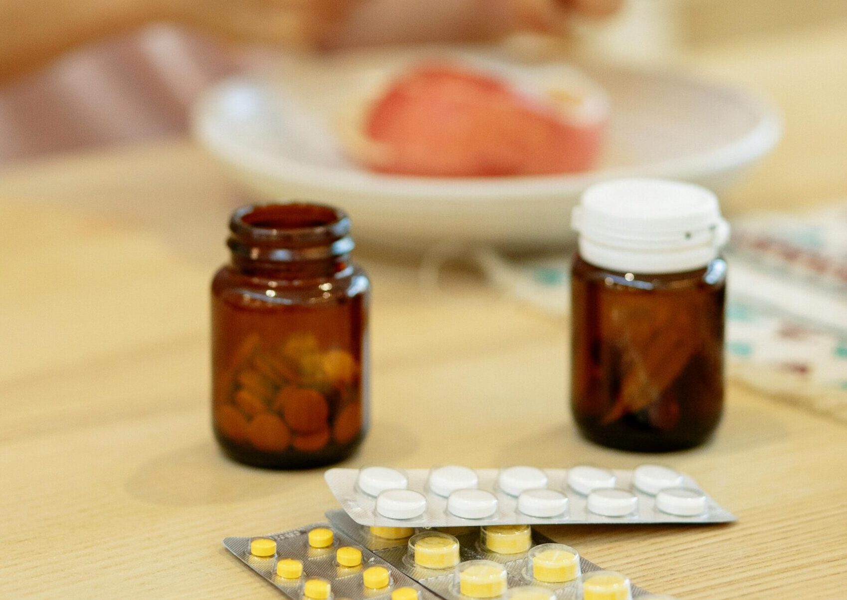 A woman peels an apple near medicine bottles on a kitchen table.