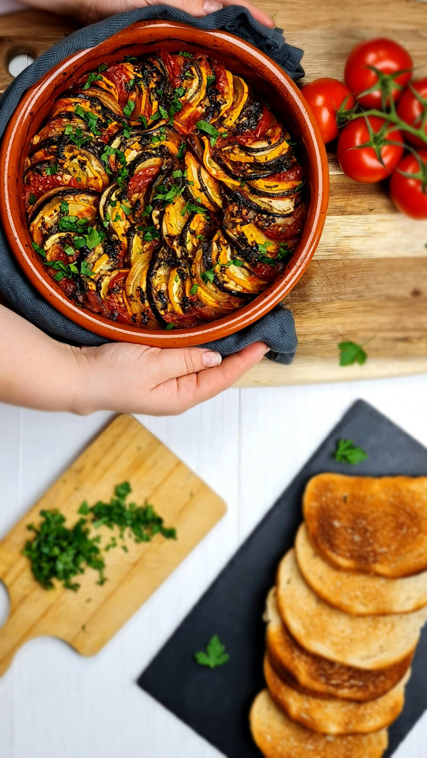 Colorful homemade ratatouille in a ceramic bowl with tomatoes and toast, perfect for a rustic meal.